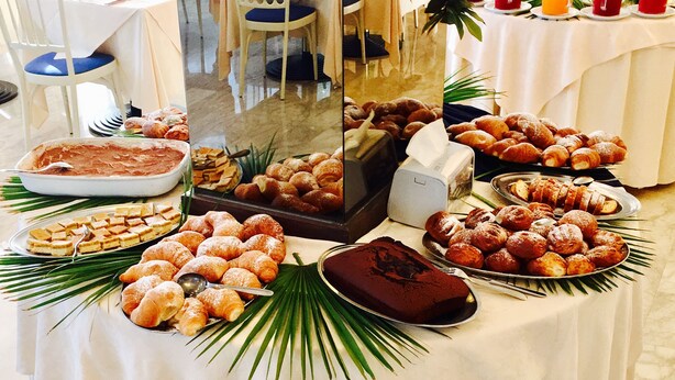 Une table de buffet proposant une variété de viennoiseries et de desserts, notamment des croissants, des pâtisseries et un gâteau au chocolat, disposés sur une nappe blanche ornée de feuilles de palmier.