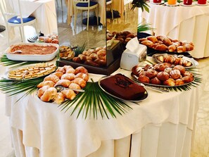 Une table de buffet proposant une variété de viennoiseries et de desserts, notamment des croissants, des pâtisseries et un gâteau au chocolat, disposés sur une nappe blanche ornée de feuilles de palmier.