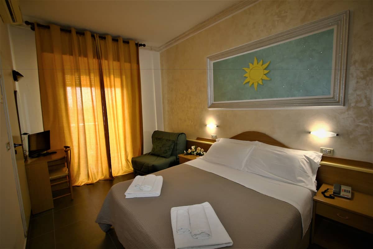 A hotel room with a bed, a desk with a television, a chair, and a nightstand with a phone.