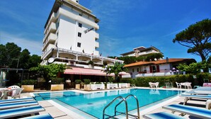 Un hôtel doté d’une piscine, de chaises longues et d’un auvent rouge et blanc.