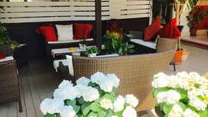 Un espace extérieur aménagé avec des meubles en osier, des coussins blancs et des plantes en pot.