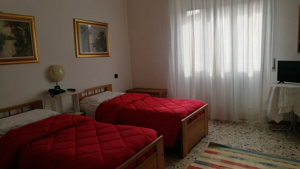 A room with two single beds, a desk with a chair, a television, and a window with sheer curtains. - Albergo Ristorante Roma (Legnano)