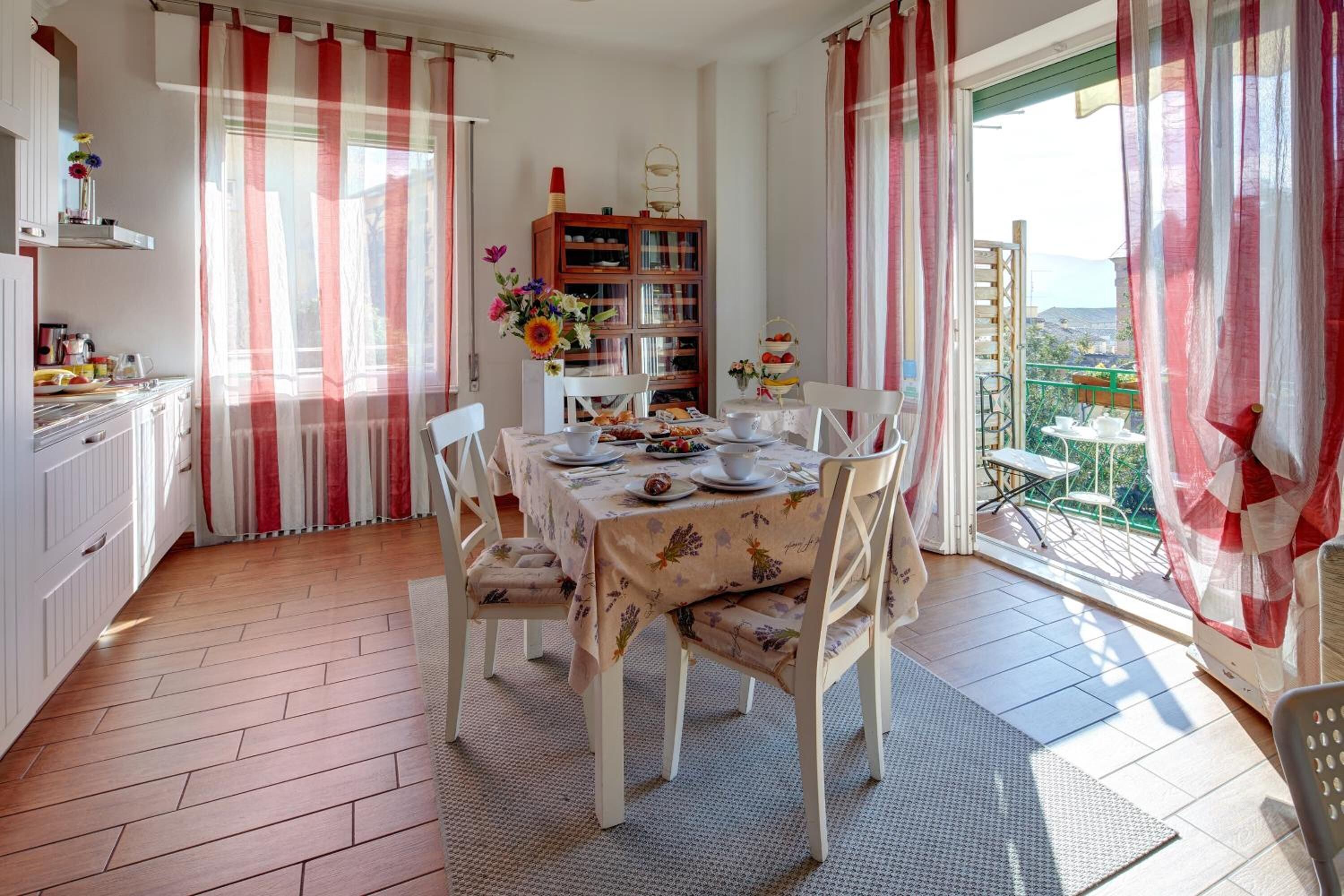 Un comedor con una mesa dispuesta para cuatro personas, rodeada de sillas blancas. Se observa un aparador de madera con puertas de cristal en el fondo.