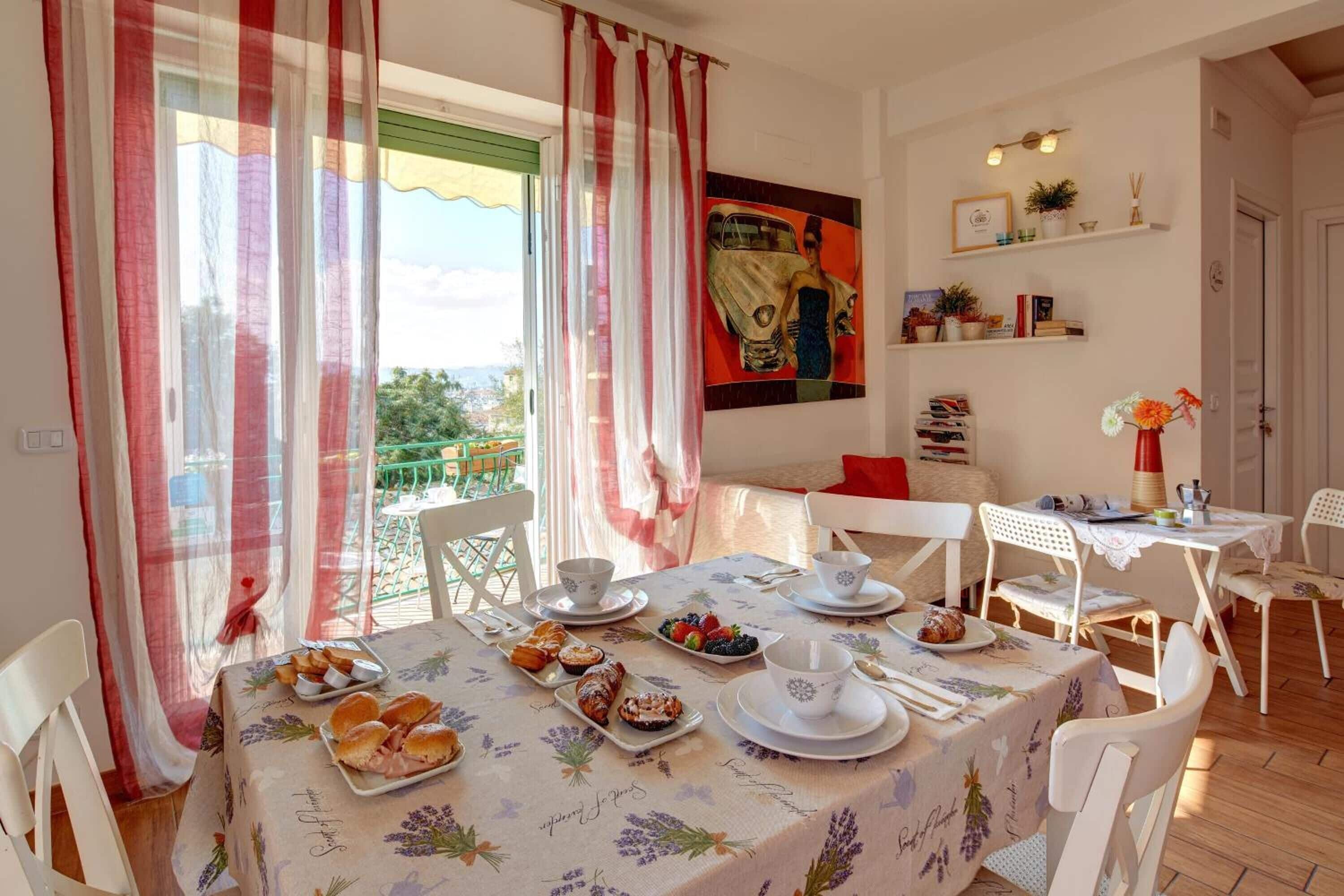 Un comedor con una mesa dispuesta para el desayuno, incluyendo bollería y frutas, con vistas a zonas verdes.