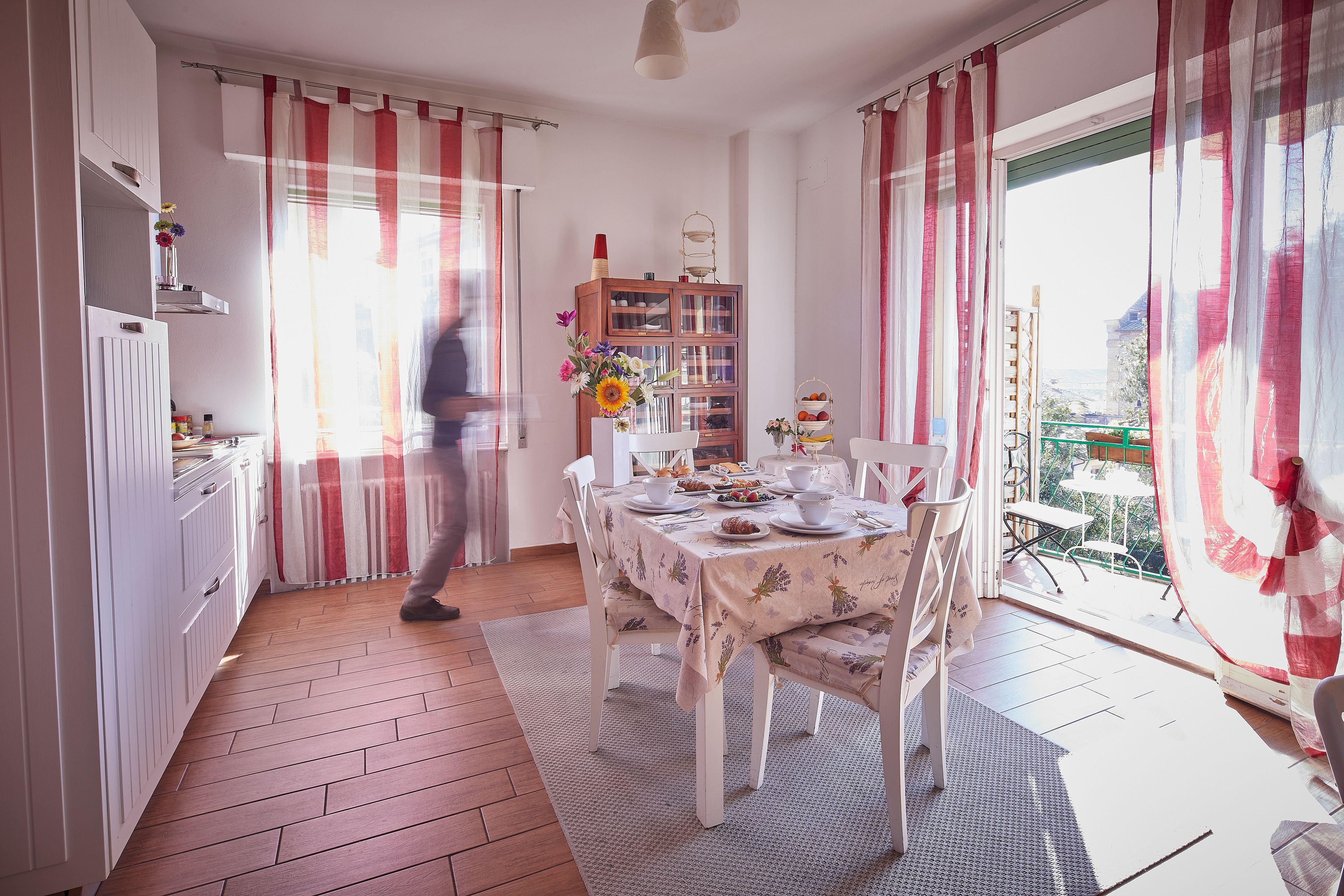A dining area with a table set for four, a wooden cabinet with glass doors, and a view through the window.