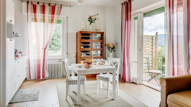 A bright dining area with a white table, chairs, and a bookshelf. A window with curtains allows natural light, and a door leads to an outdoor balcony. - Cento Passi Dal Duomo (Arezzo)