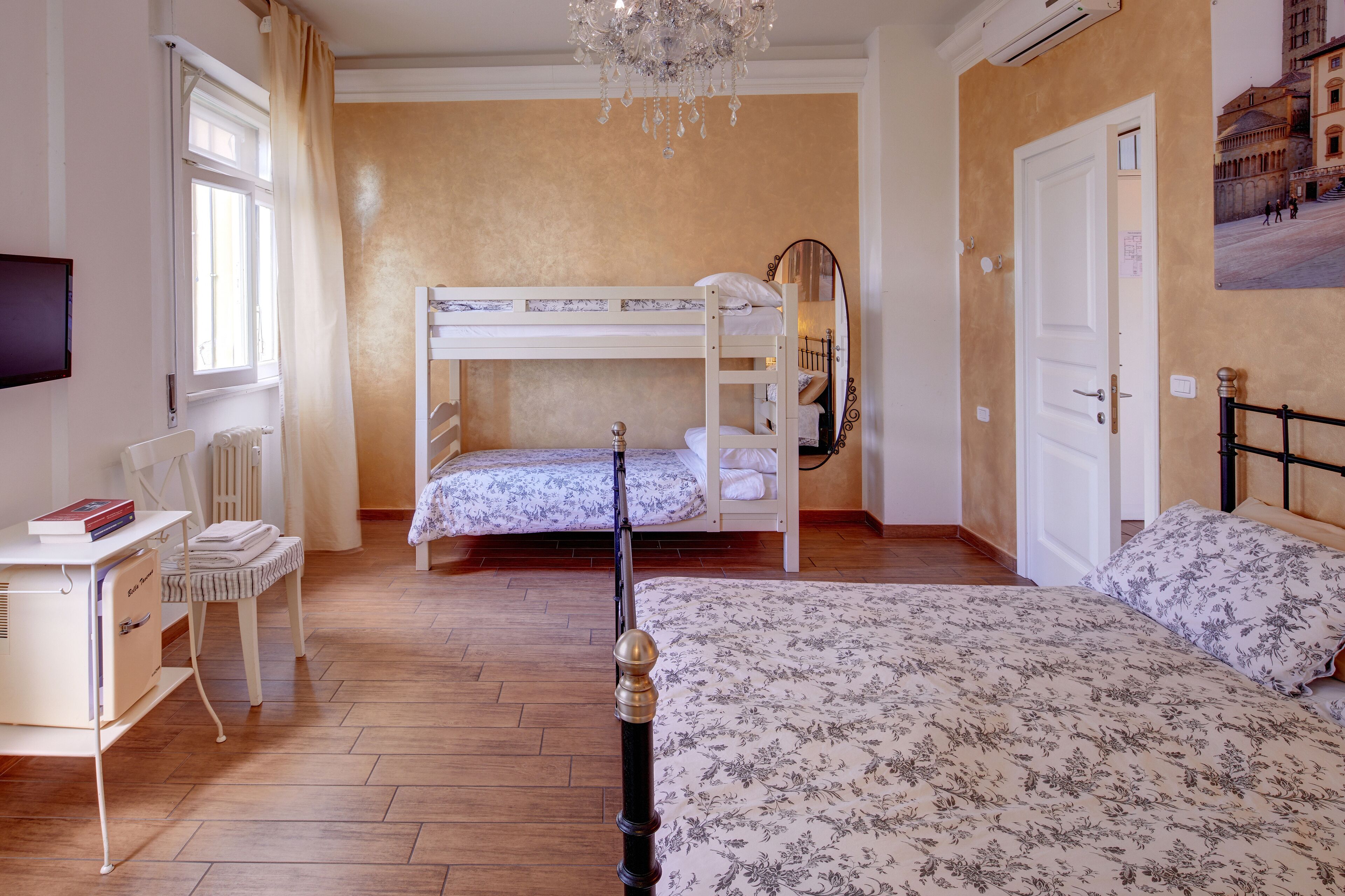 Een slaapkamer met een stapelbed, een bureau met stoel, een radiator en een kroonluchter.