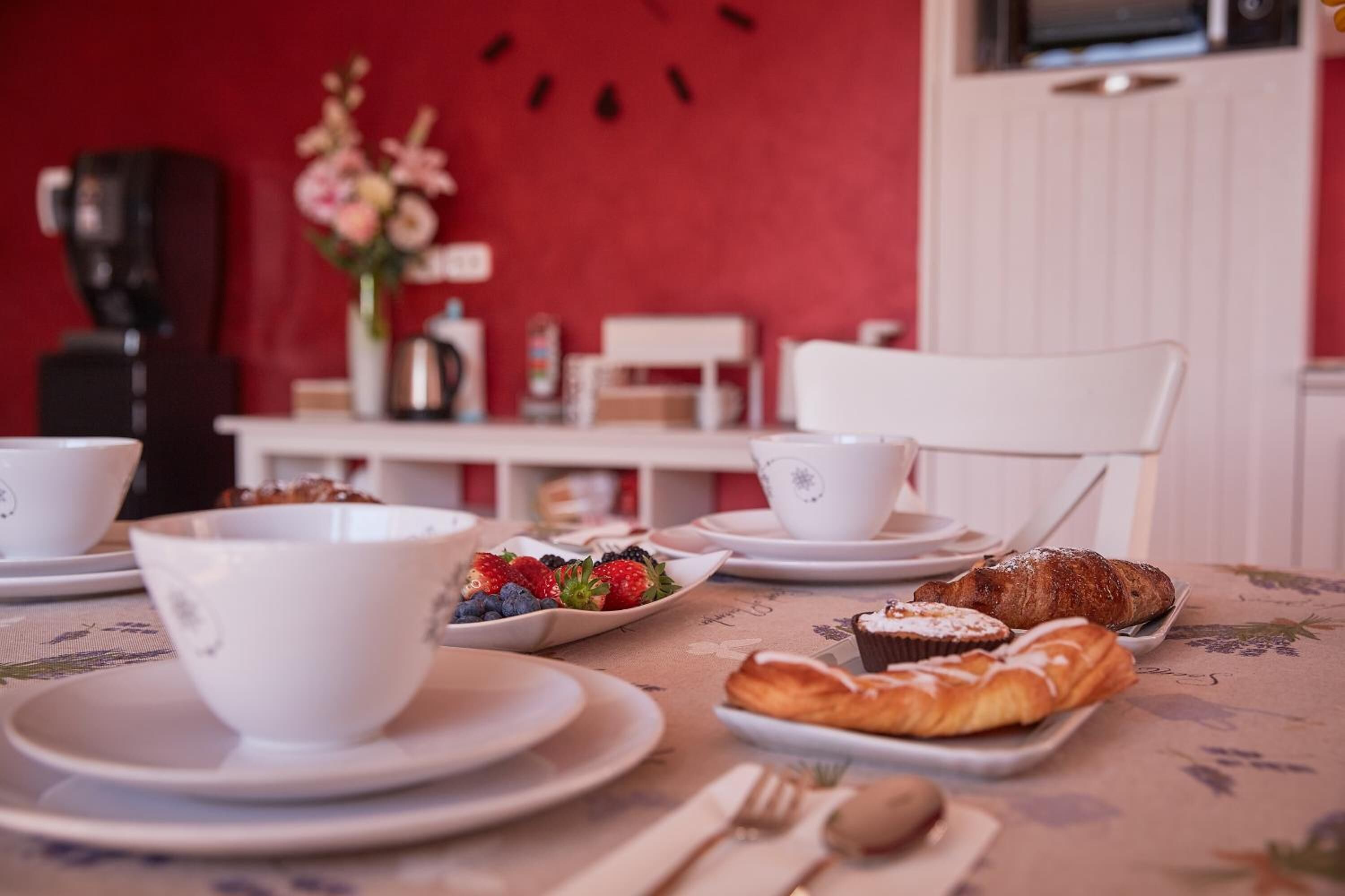 Ein Frühstückstisch mit Tellern voller Gebäck und Früchten, weißen Tassen und einer Kaffeemaschine.