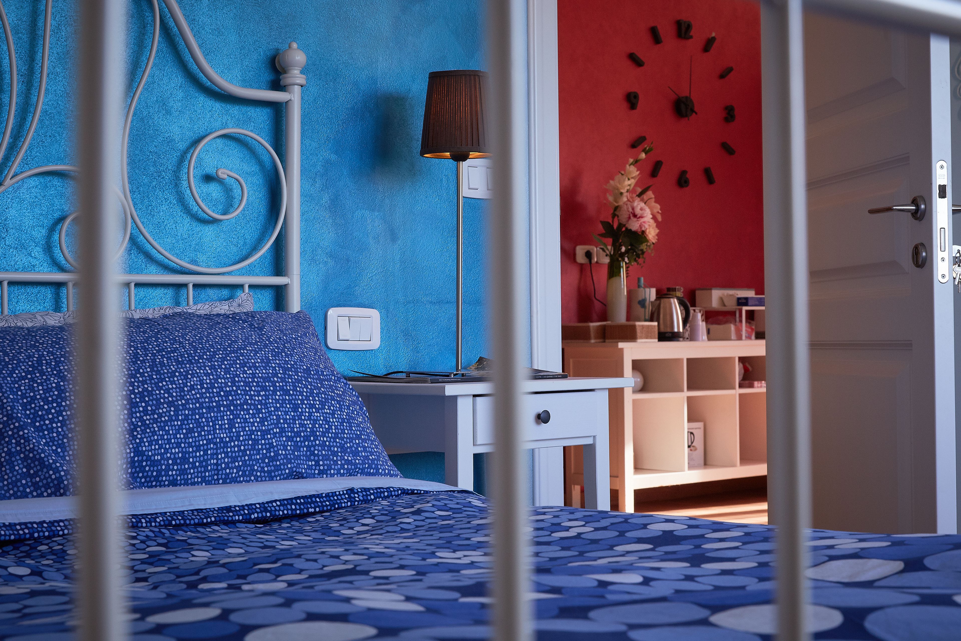 Un dormitorio con cama, mesita de noche, lámpara, reloj y puerta.