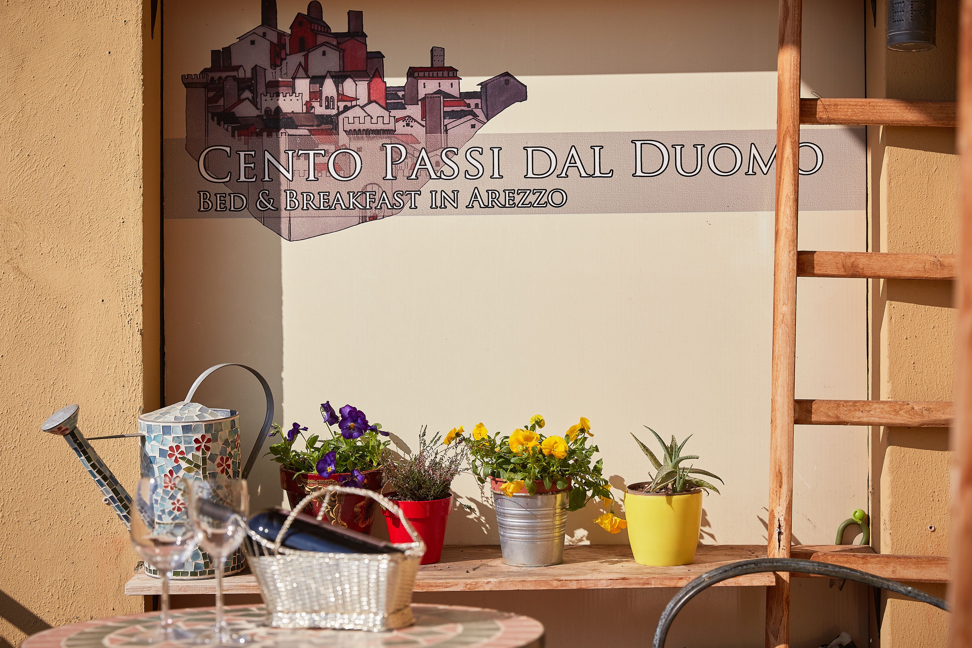 Une enseigne indiquant le « Centro Passi Dal Duomo », un bed and breakfast situé à Arezzo, avec des plantes en pot et un arrosoir sur une table.