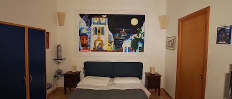 Un dormitorio con una cama, un cuadro con un cielo nocturno, una puerta de madera y un armario azul.