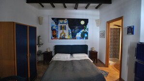 A bedroom with a bed, a wardrobe, a nightstand, a painting on the wall, and a door leading to another room. - Ambra (Lipari)