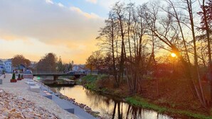 A riverside walkway with a stone path, a bridge, and trees reflecting the sunset. - Hotel Well Garni (Wittlich)