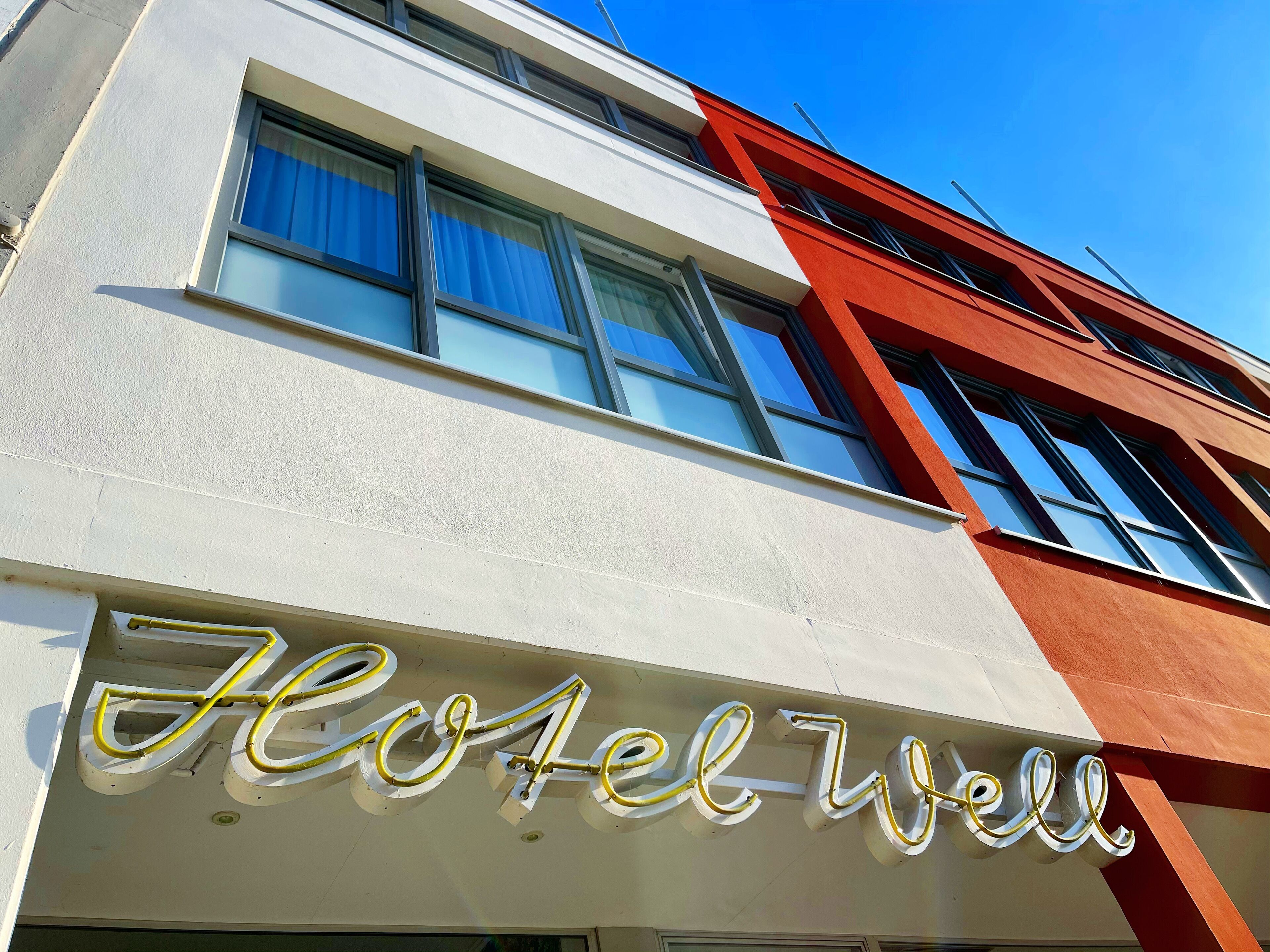 La façade d’un hôtel au design moderne, caractérisée par de grandes fenêtres et une enseigne bien visible indiquant « Hôtel Well ».