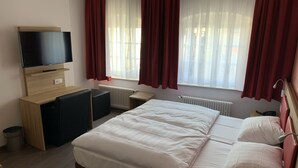A hotel room with a bed, a TV, a desk, and a window with curtains. - Hotel Well Garni (Wittlich)