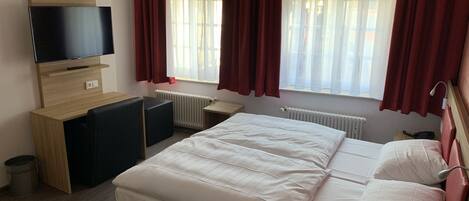A hotel room with a bed, a TV, a desk, and a window with curtains.