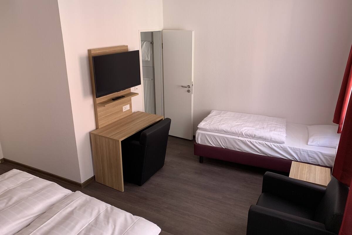 A hotel room with a wooden desk, a television, two beds, and a wardrobe.