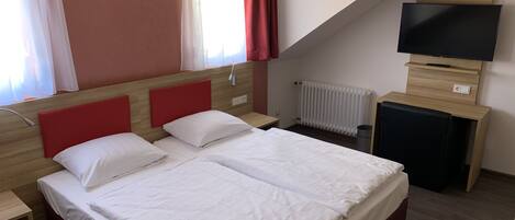 A hotel room with two beds, a TV, a desk, and a radiator.