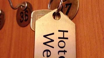 Una tarjeta de llave de hotel con la inscripción "Hotel Well" sujeta a un llavero, colgando de una puerta con manija de bronce y una placa con el número 36.