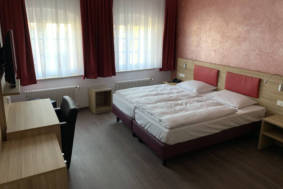A hotel room with a bed, desk, chair, and a window with curtains.