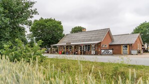A traditional brick building with a covered front area, likely a pub or restaurant, with outdoor seating and a sign indicating it serves food and drinks. - Knaplund Destillery (Tarm)