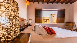 Ein Schlafzimmer mit Bett, Holz-Kopfteil, Fenster mit Fensterläden und einer Steinwand.