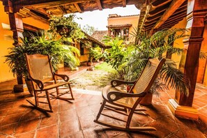 A courtyard with two rocking chairs, surrounded by lush tropical plants and a traditional building with a tiled roof. - La Casa Amarilla (Mompos)