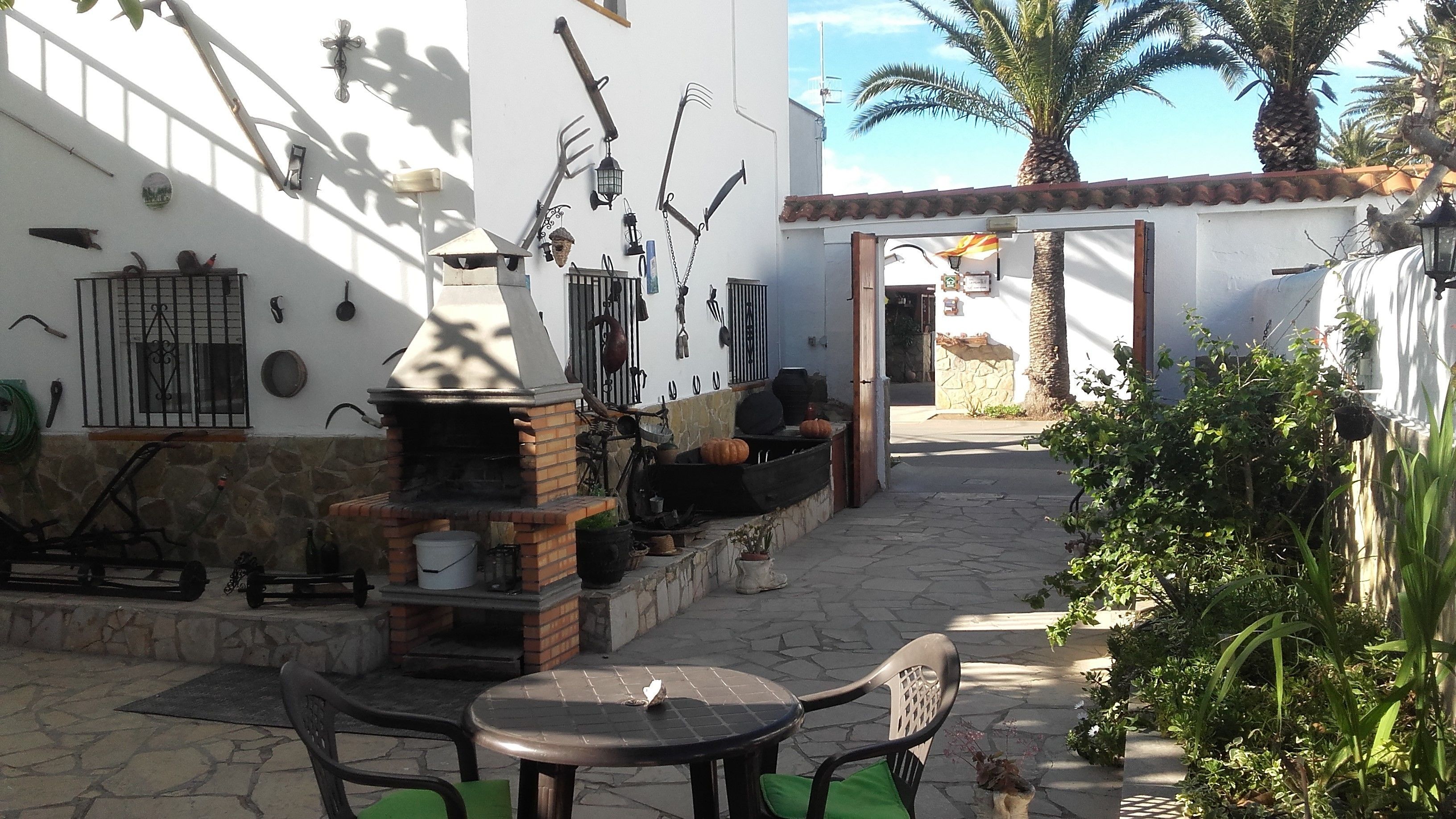 An outdoor patio with a brick oven, seating area, and various gardening tools on the wall.