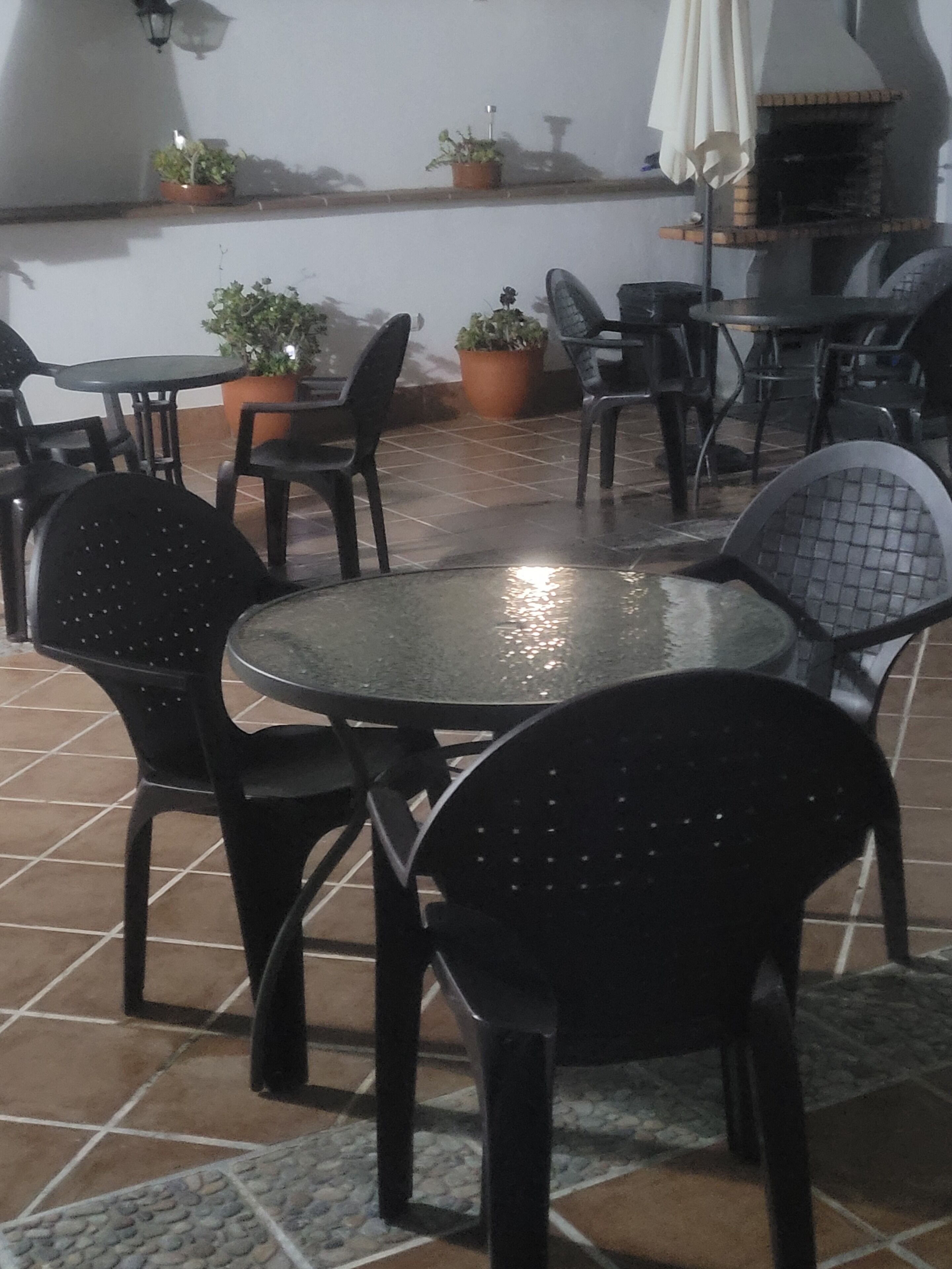 An outdoor patio area with a round table and chairs, potted plants, and a grill.