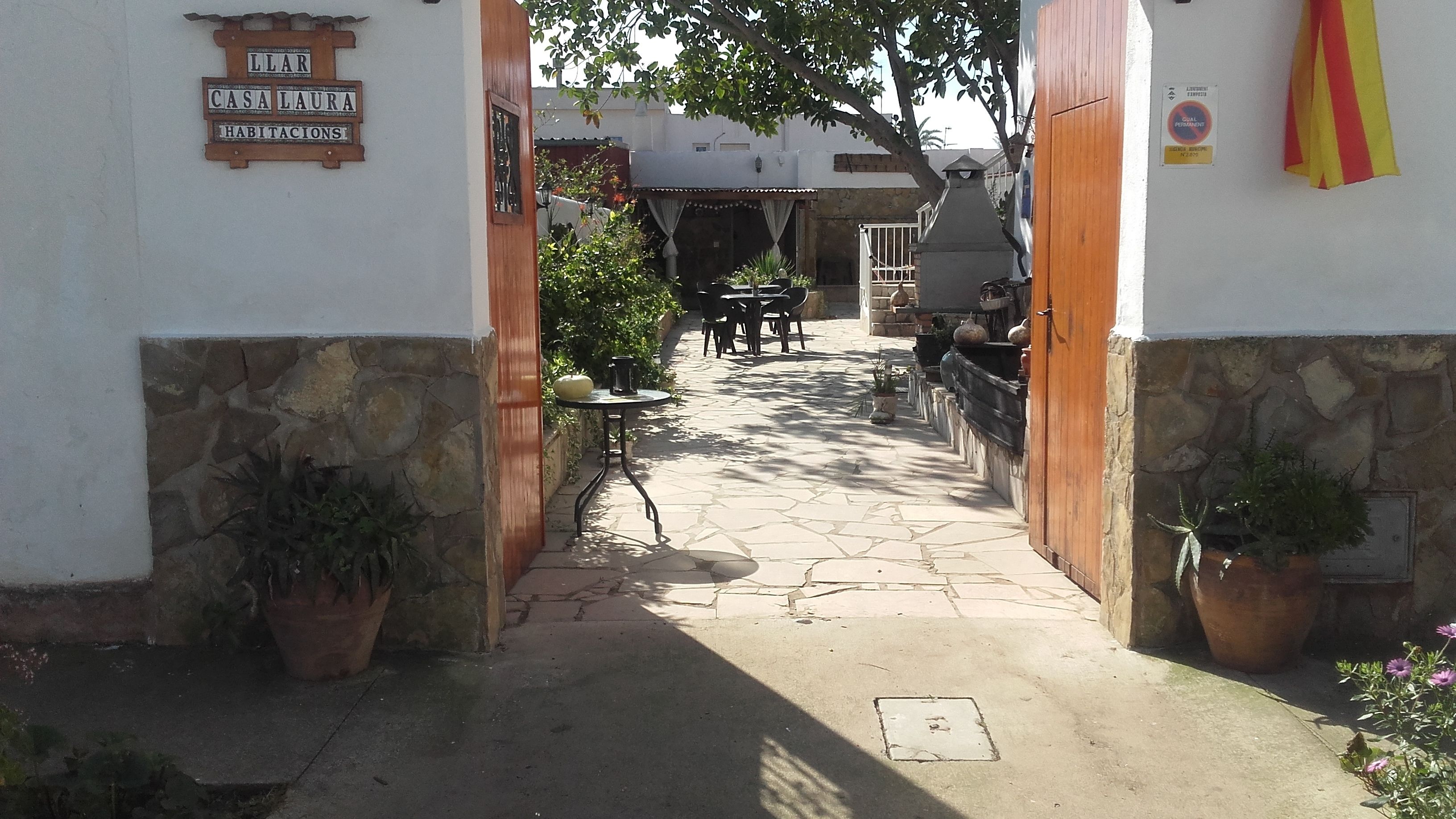 Un patio empedrado con puerta de madera, plantas en macetas y un cartel que indica 'Casa Laura Habitats'.