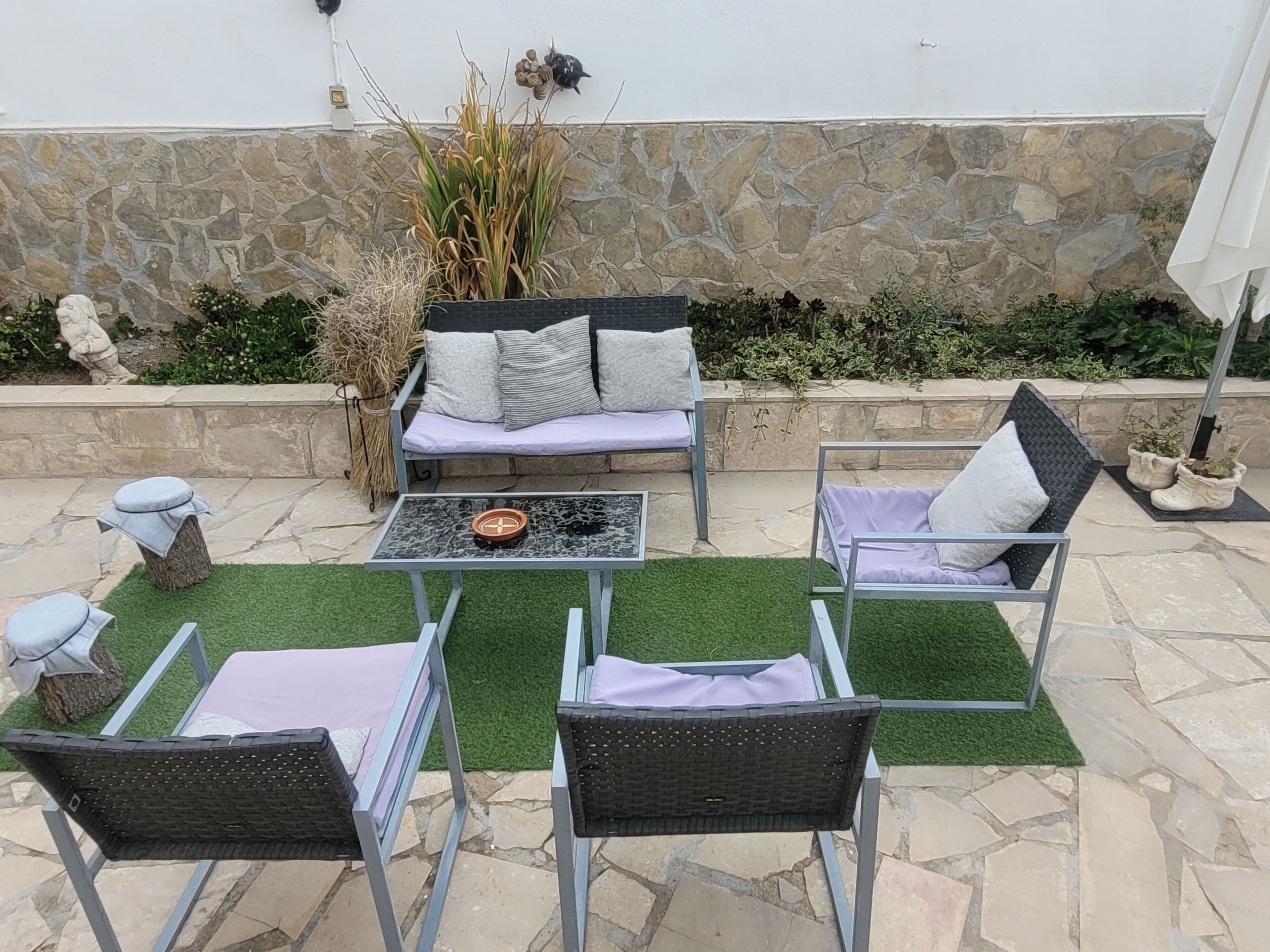 Een terras buiten met een stenen muur, een bank, twee stoelen, een tafel en sierplanten.