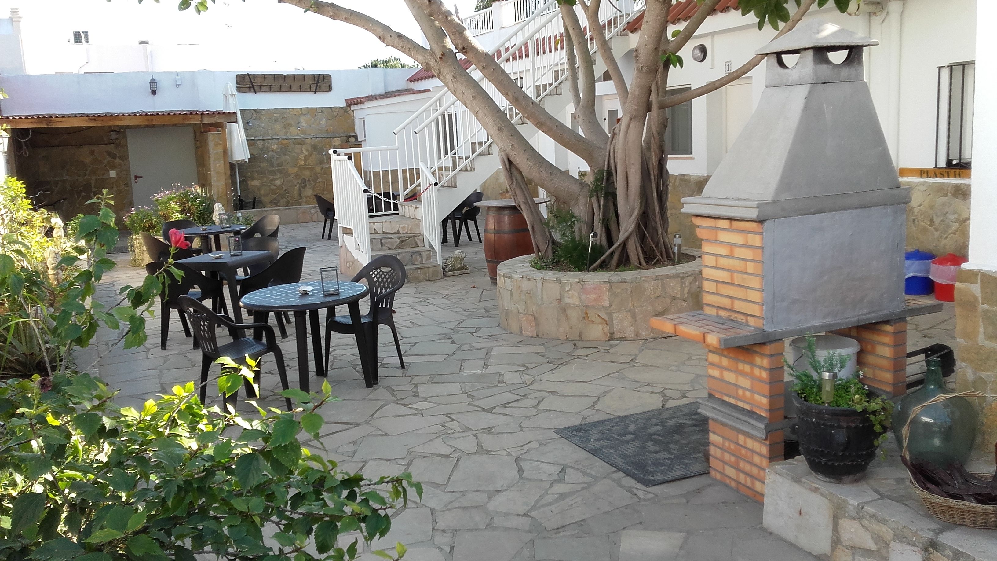An outdoor patio with stone flooring, a barbecue grill, and several tables and chairs.