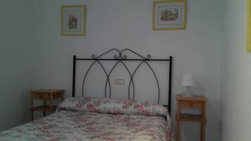 Un lit recouvert d’une couvre-lit à motifs floraux, deux tables de chevet, une lampe fixée au mur et deux tableaux encadrés accrochés au mur.