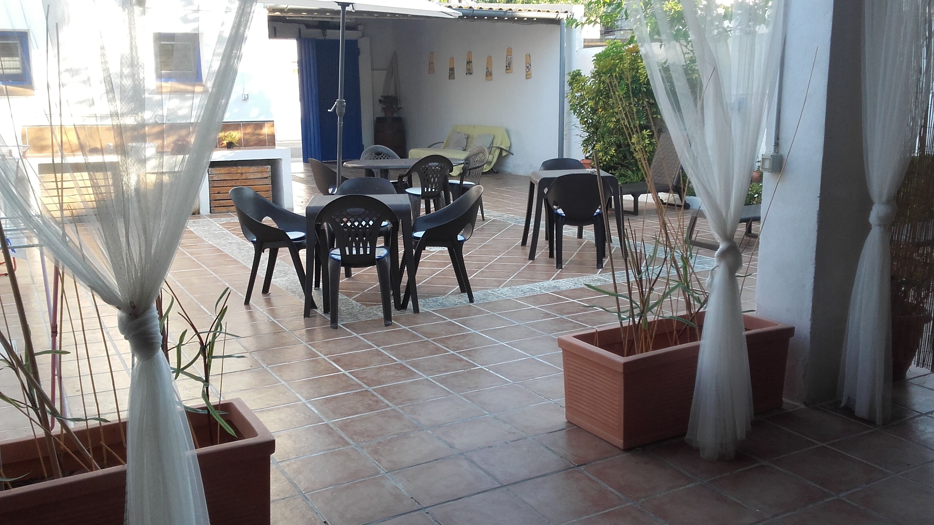 Un patio al aire libre con una mesa y sillas, rodeado de macetas con plantas y un suelo de baldosas.