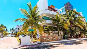 Un hotel moderno con un llamativo letrero que dice 'CASA DE MAR', que presenta una fachada curva, varios balcones y está rodeado de palmeras.