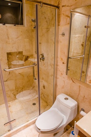 A bathroom with a glass-enclosed shower, a white toilet, and a marble-tiled wall.