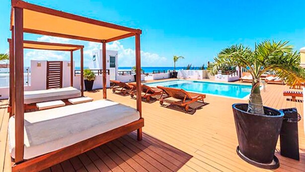 Una terraza de madera con una cama con dosel, sillas de descanso, una piscina y plantas en macetas.