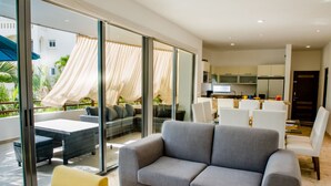 Una sala moderna con un sofá gris, un sillón amarillo y un comedor con sillas blancas.