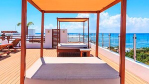 Una terraza de madera con un toldo, un área de piscina y vista al océano.