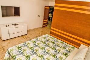 A bedroom with a bed, a TV mounted on the wall, a white dresser, and a wooden headboard.