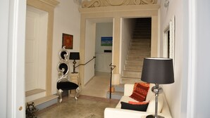 A living room with a white sofa, a red throw pillow, a lamp, and a staircase leading to another room. - Up Room & Suite (Lecce)