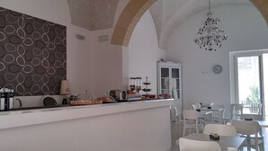 A modern kitchen with a breakfast bar, a chandelier, and a dining area with white chairs and tables. - Up Room & Suite (Lecce)