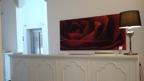 A reception area with a white reception desk, a large red artwork above it, and a floor lamp to the right. - Up Room & Suite (Lecce)