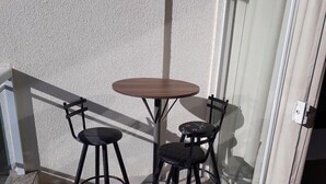 A small outdoor seating area with a table and two chairs, a textured wall, and a glass door. - Atrium - Achei Ferias (Caldas Novas)