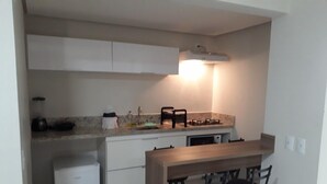 A compact kitchen with a countertop, a sink, a stove, and a refrigerator. There are three bar stools and a wooden table. - Atrium - Achei Ferias (Caldas Novas)