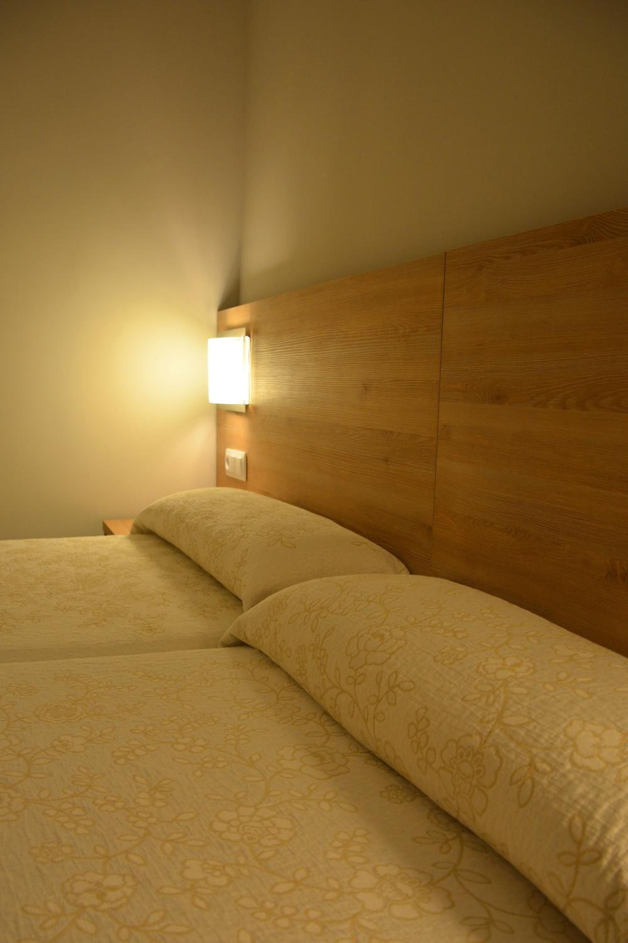 Una habitación de hotel con cabecera de madera, dos camas con ropa de cama de estampado floral y una lámpara fijada a la pared.