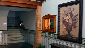 A hallway with a staircase, a wooden bench, a potted plant, and a framed painting on the wall.