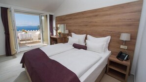 A double bed with a wooden headboard, bedside tables with lamps, and a view of the sea through an open door. - Biokovka (Makarska)