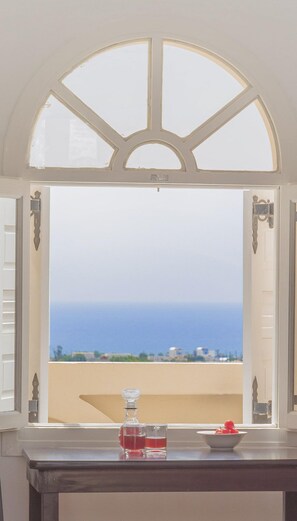 Vista a través de una ventana con marco blanco y un arco decorativo. En el interior, hay una mesa con un vaso, un cuenco pequeño y una botella.