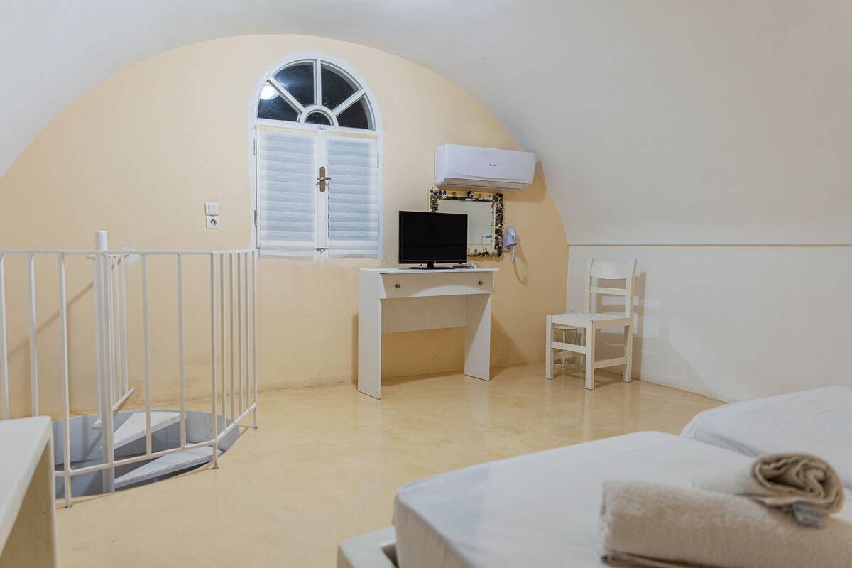 A room with a bed, a desk with a computer, a chair, a window, and a staircase.